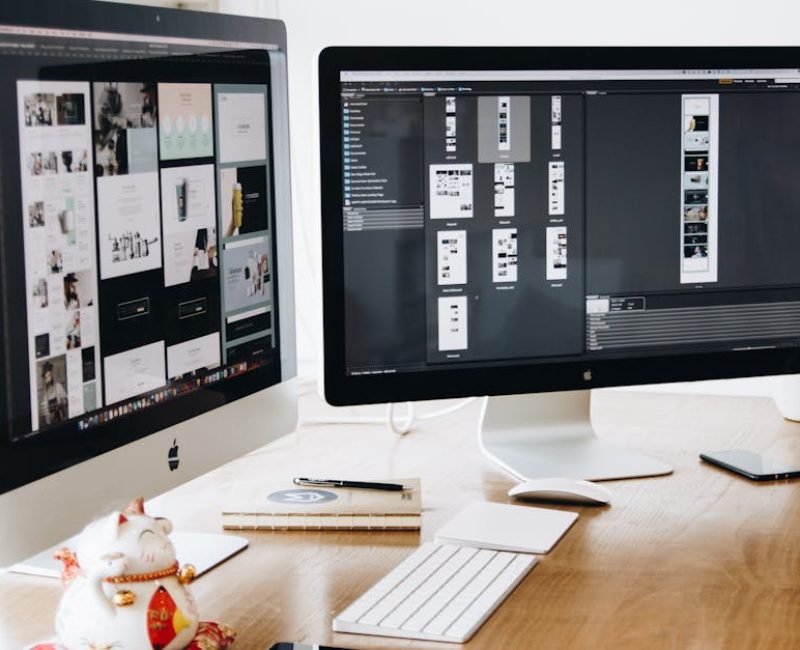 Two Imac's With Keyboard and Phones on Desk